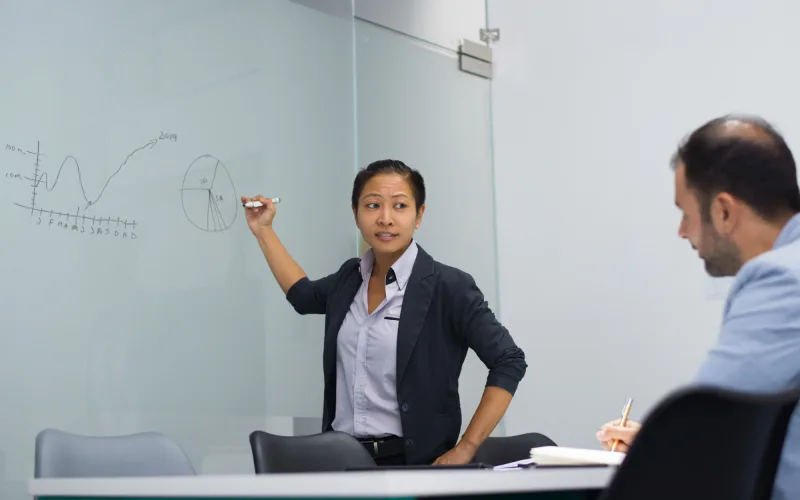 An instructor presenting data charts on a whiteboard to a delegate
